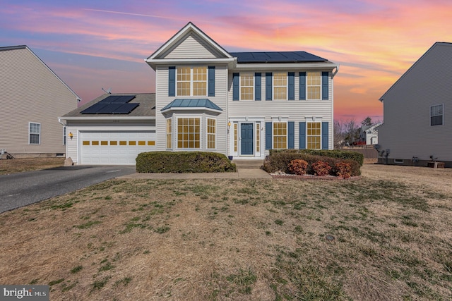 view of front of home with a yard, roof mounted solar panels, a standing seam roof, a garage, and driveway