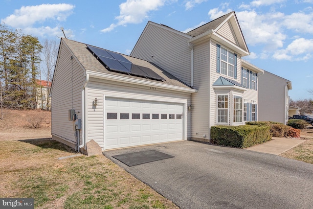 view of front of property featuring driveway, a garage, and roof mounted solar panels