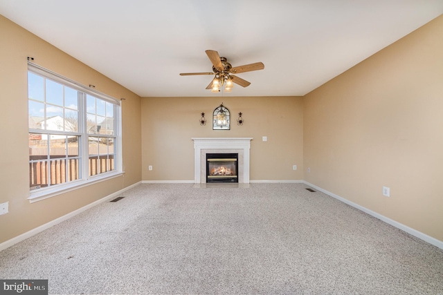 unfurnished living room featuring carpet flooring, a fireplace with flush hearth, baseboards, and ceiling fan