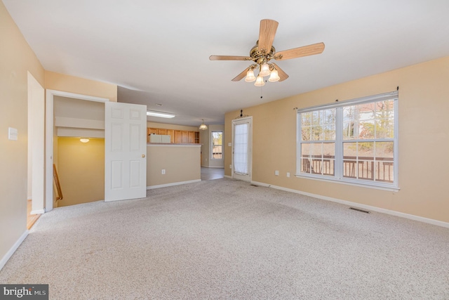 interior space with baseboards, visible vents, a ceiling fan, and light colored carpet