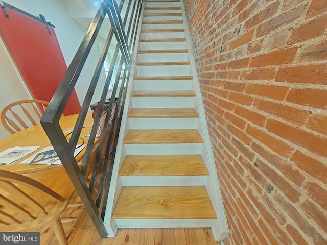 stairway featuring brick wall, wood finished floors, and a barn door