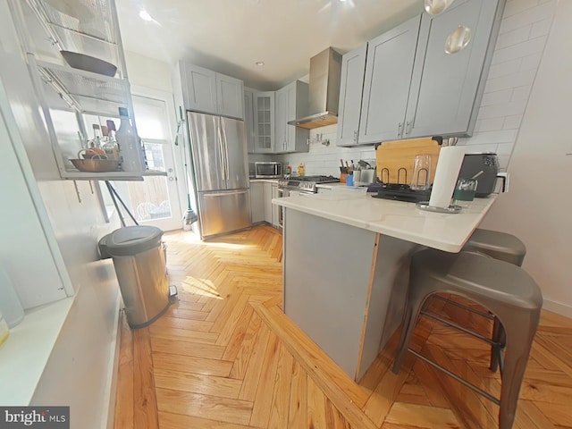 kitchen with decorative backsplash, wall chimney exhaust hood, a peninsula, gray cabinets, and stainless steel appliances