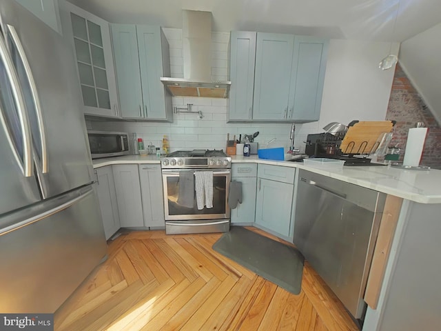 kitchen featuring stainless steel appliances, backsplash, wall chimney range hood, light stone countertops, and a peninsula