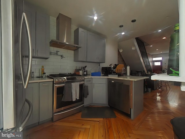 kitchen with a peninsula, light countertops, appliances with stainless steel finishes, decorative backsplash, and wall chimney exhaust hood