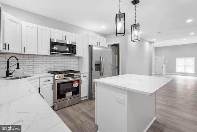 kitchen featuring light stone counters, appliances with stainless steel finishes, white cabinets, a sink, and a kitchen island