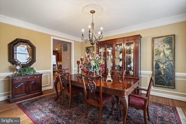 dining room with ornamental molding, wainscoting, a notable chandelier, and wood finished floors