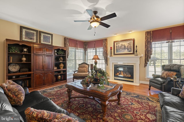 living room featuring a glass covered fireplace, a ceiling fan, and light wood-style floors