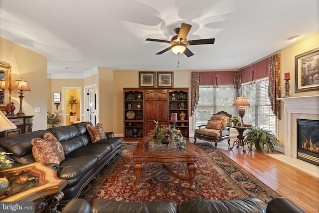 living area with ceiling fan, wood finished floors, and a glass covered fireplace