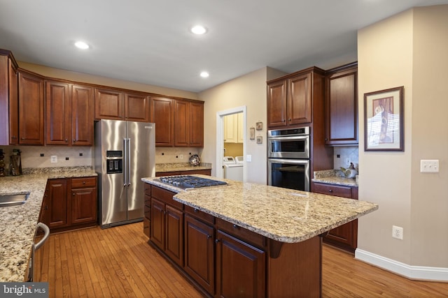 kitchen featuring stainless steel appliances, a kitchen island, backsplash, light wood finished floors, and washing machine and clothes dryer