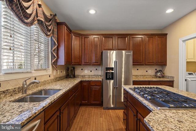 kitchen featuring decorative backsplash, light stone counters, stainless steel appliances, light wood-type flooring, and a sink