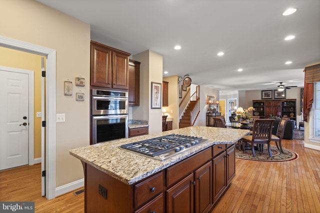 kitchen featuring light stone counters, open floor plan, a center island, stainless steel appliances, and light wood-type flooring