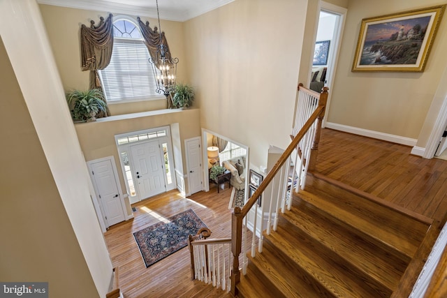 entryway featuring baseboards, a towering ceiling, ornamental molding, wood finished floors, and a notable chandelier