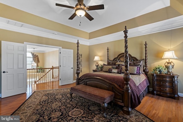 bedroom featuring wood finished floors, visible vents, baseboards, a tray ceiling, and crown molding