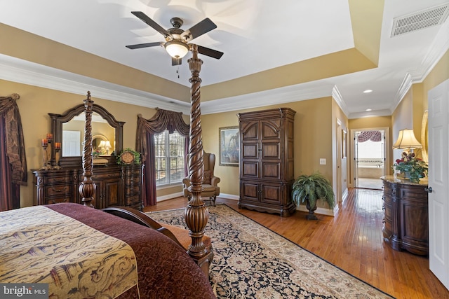 bedroom featuring baseboards, visible vents, a raised ceiling, wood finished floors, and crown molding