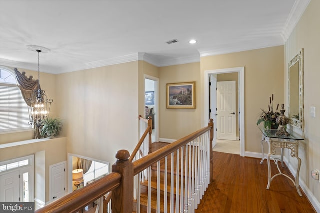 hallway with a notable chandelier, wood finished floors, visible vents, an upstairs landing, and ornamental molding