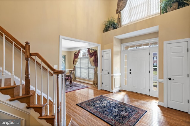 foyer entrance featuring crown molding, a high ceiling, wood finished floors, baseboards, and stairs