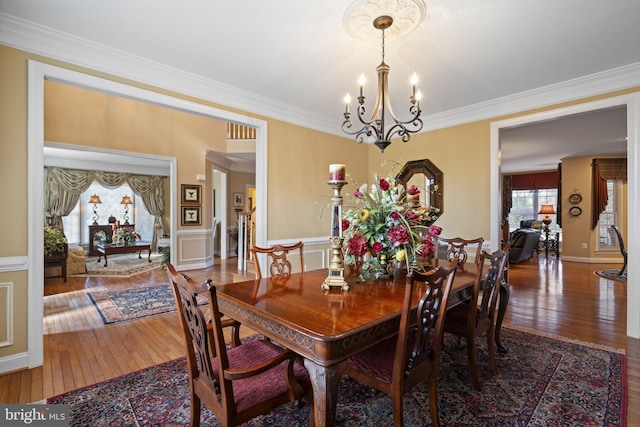 dining space with wainscoting, an inviting chandelier, wood finished floors, and crown molding