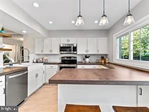 kitchen with stainless steel appliances, a peninsula, white cabinets, and hanging light fixtures