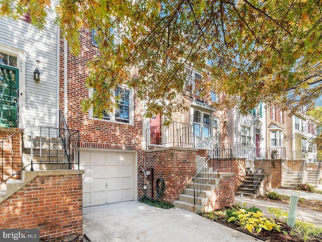 townhome / multi-family property featuring stairway, brick siding, a garage, and driveway