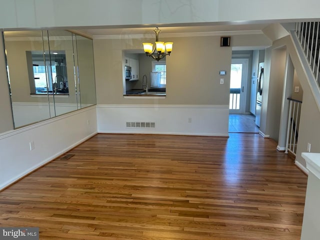 unfurnished dining area featuring visible vents, a notable chandelier, ornamental molding, a sink, and wood finished floors