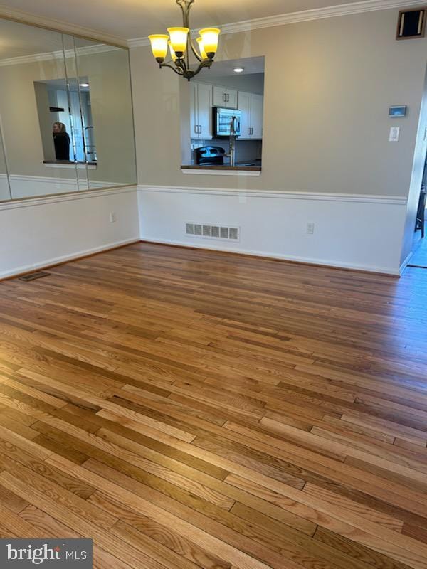 unfurnished dining area featuring visible vents, an inviting chandelier, wood finished floors, and ornamental molding