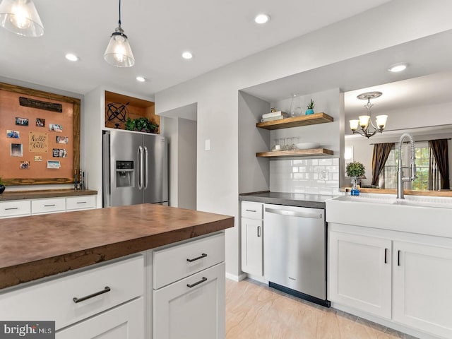 kitchen featuring tasteful backsplash, white cabinets, stainless steel appliances, wood counters, and a sink