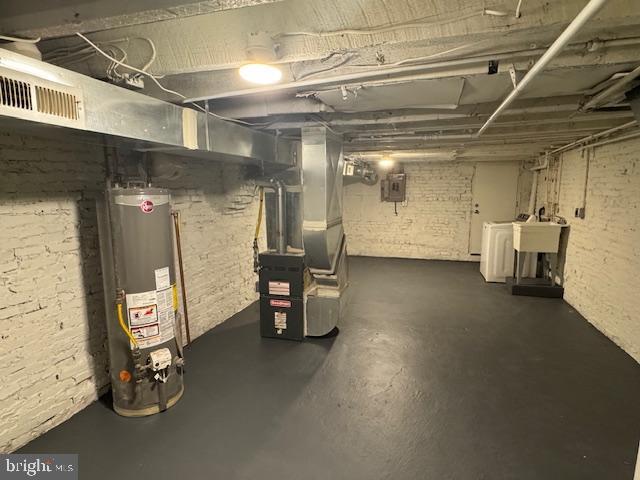 basement featuring electric panel, separate washer and dryer, water heater, brick wall, and heating unit