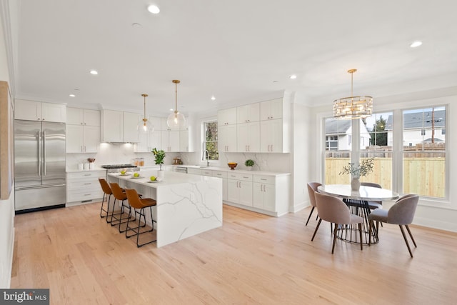 kitchen featuring decorative light fixtures, a kitchen island, white cabinets, and stainless steel built in fridge