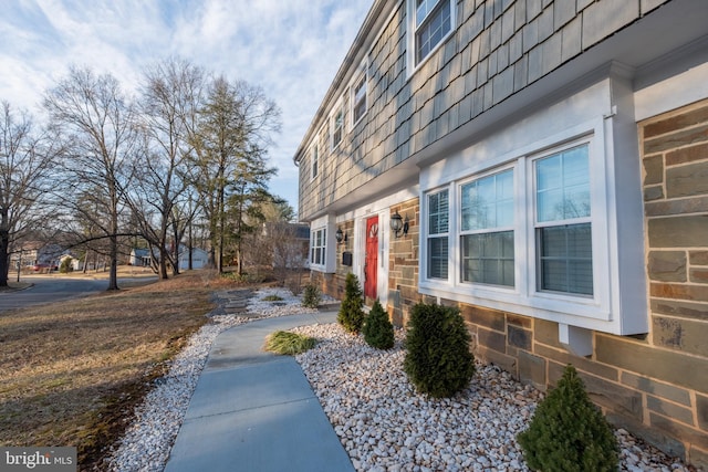 view of side of property with stone siding and mansard roof