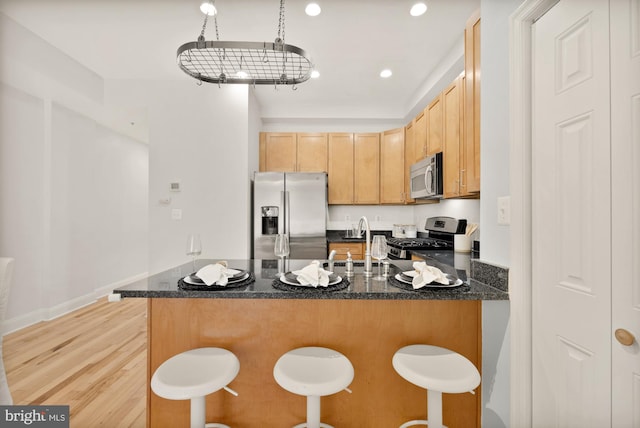 kitchen featuring light wood finished floors, dark stone countertops, a peninsula, stainless steel appliances, and a sink