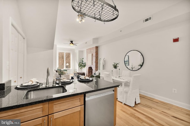 kitchen featuring a sink, visible vents, light wood-style floors, dishwasher, and dark stone countertops