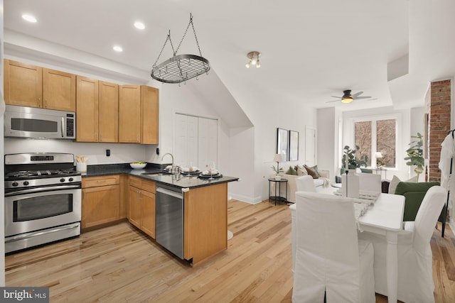 kitchen with a peninsula, a sink, open floor plan, appliances with stainless steel finishes, and dark countertops