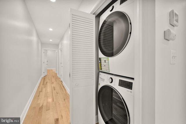 laundry room with baseboards, laundry area, stacked washer and clothes dryer, and light wood-style floors