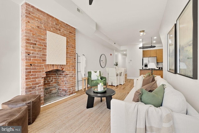 living room with recessed lighting, visible vents, baseboards, light wood-style floors, and a brick fireplace