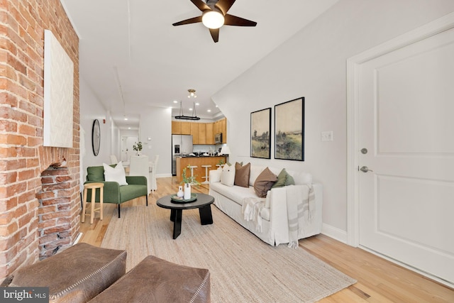 living area with recessed lighting, light wood-style flooring, ceiling fan, brick wall, and baseboards