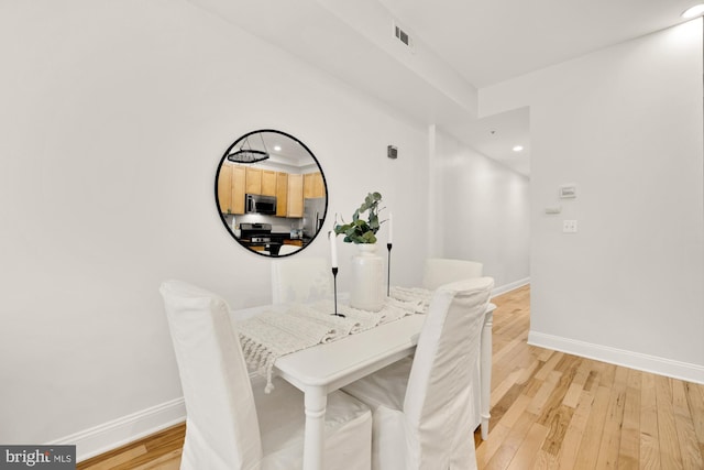 dining area with light wood-type flooring, visible vents, and baseboards