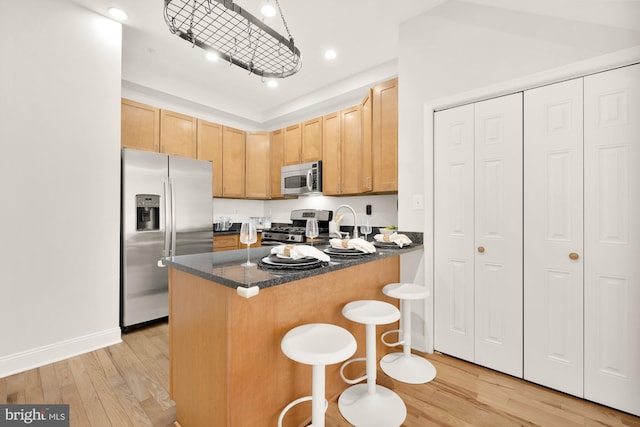 kitchen featuring appliances with stainless steel finishes, a kitchen breakfast bar, dark stone countertops, light wood-type flooring, and light brown cabinets