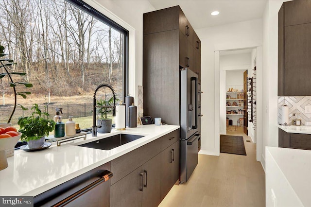 kitchen with stainless steel appliances, light countertops, a sink, dark brown cabinets, and light wood-type flooring