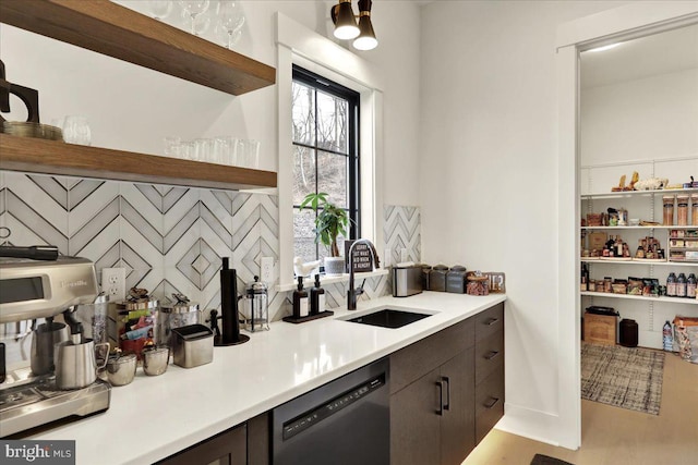 kitchen with dark brown cabinetry, dishwasher, wood finished floors, light countertops, and a sink