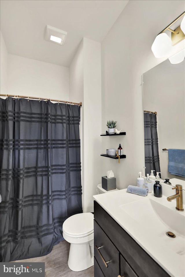 bathroom with toilet, wood finished floors, vanity, and a shower with curtain