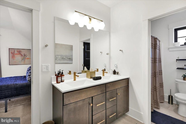 full bath with double vanity, toilet, ensuite bathroom, a sink, and baseboards