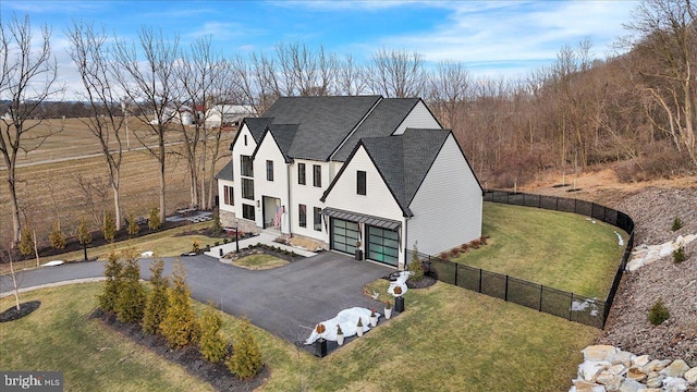 view of front of home with aphalt driveway, roof with shingles, a front yard, and fence