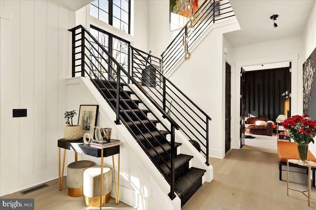 stairway featuring wooden walls, a high ceiling, visible vents, and wood finished floors