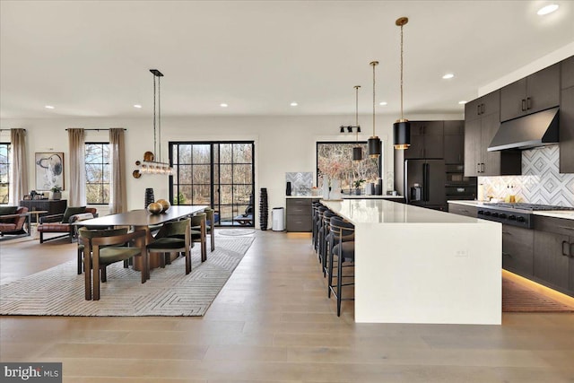 kitchen featuring stainless steel gas stovetop, hanging light fixtures, light countertops, under cabinet range hood, and high end black refrigerator