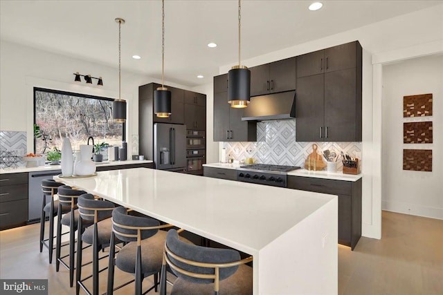 kitchen featuring a center island, decorative light fixtures, light countertops, appliances with stainless steel finishes, and under cabinet range hood