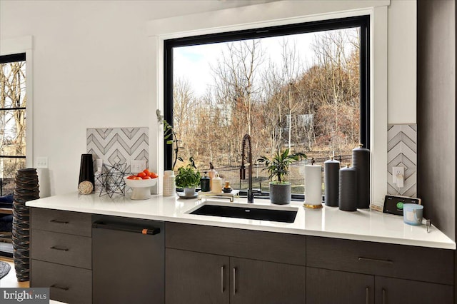 kitchen featuring dishwashing machine, light countertops, a sink, and dark brown cabinets