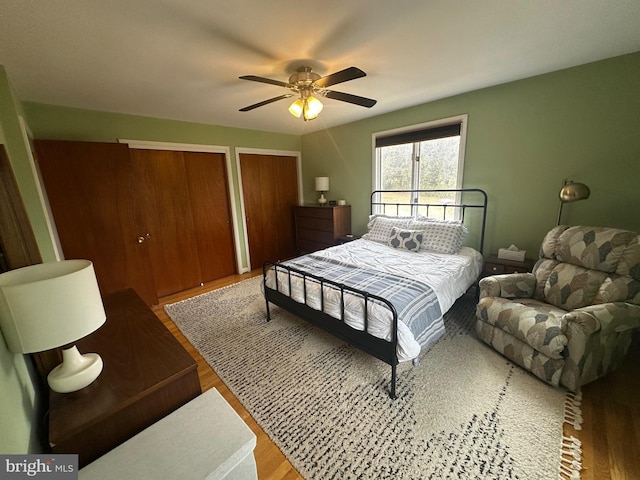 bedroom with ceiling fan, wood finished floors, and two closets