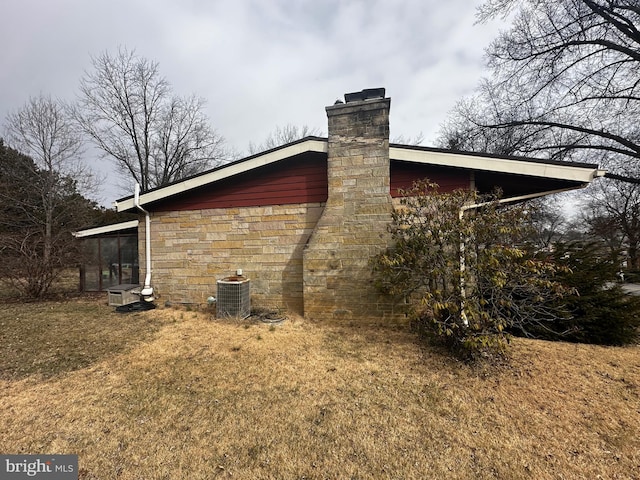 view of side of home featuring cooling unit, stone siding, a yard, and a chimney