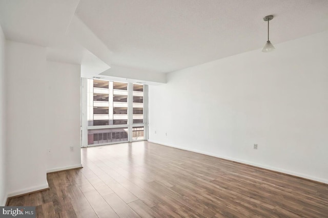 empty room featuring floor to ceiling windows, baseboards, and wood finished floors