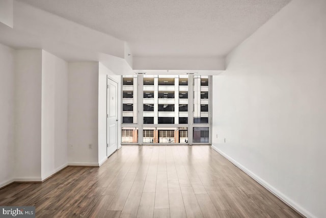 unfurnished living room with a textured ceiling, baseboards, and wood finished floors